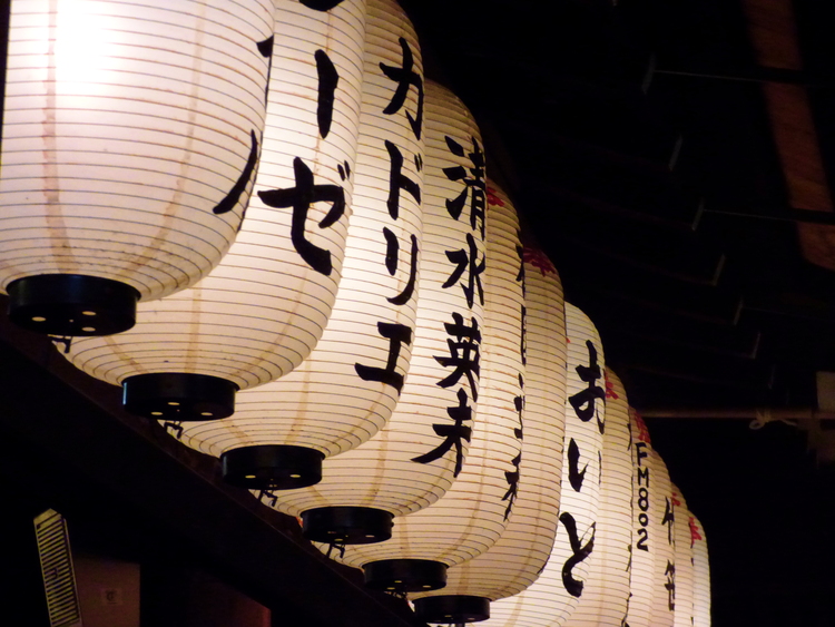 A row of white paper lanterns in the dark with black Japanese writing on them