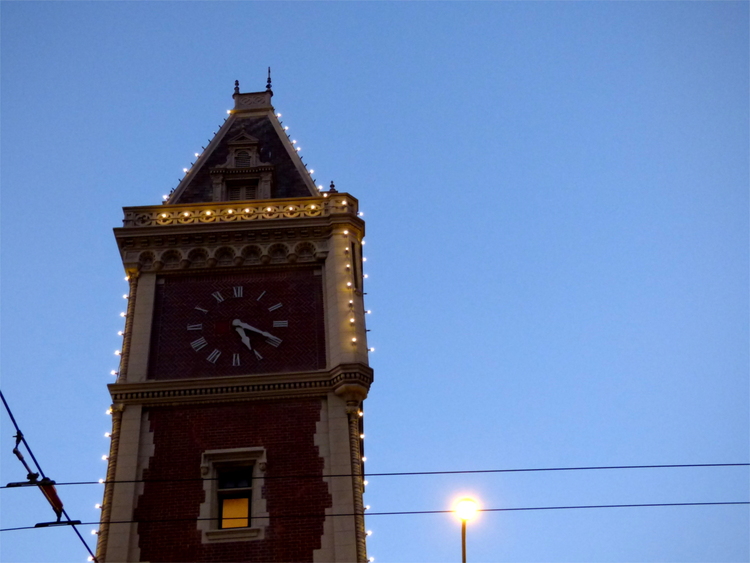 A red-brick clock-tower decorated with strings of lights