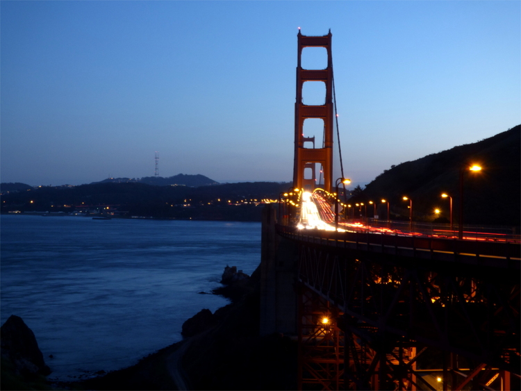 A view of the Golden Gate bridge at dusk with cars forming streaks of light across it
