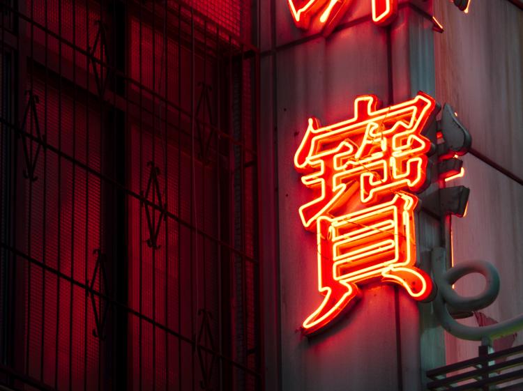 A glowing red neon sign of a Chinese character on a facade with metal window grates