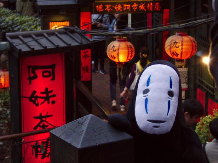 A plush toy of No-Face from the movie Spirited Away in front of the entrance to a tea house