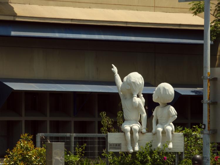 A white sculpture of two children looking curiously up towards a building