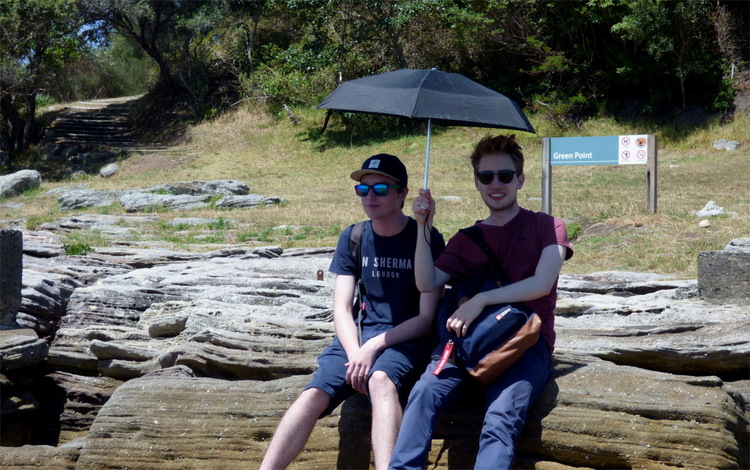 Jan and Julian sitting on some stones under an umbrella in the sun for shade