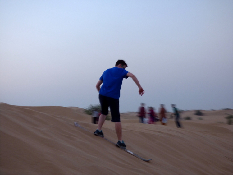 Jan surfing down a small sand dune on a skateboard without wheels