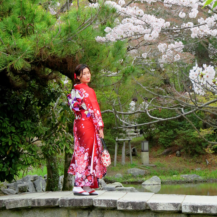 A woman in a red floral Kimono standing on a small stone bridge posing for pictures