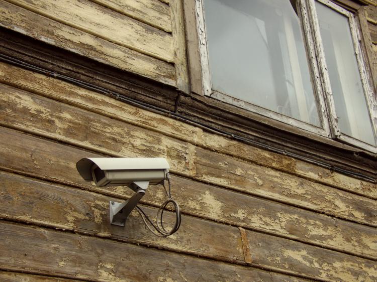 A white security camera on a withered facade made of wooden planks that might once have been painted white