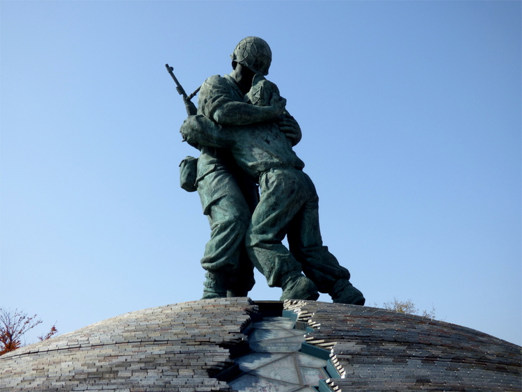 A sculpture of two soldiers in uniform hugging each other leaning over a crack in the ground