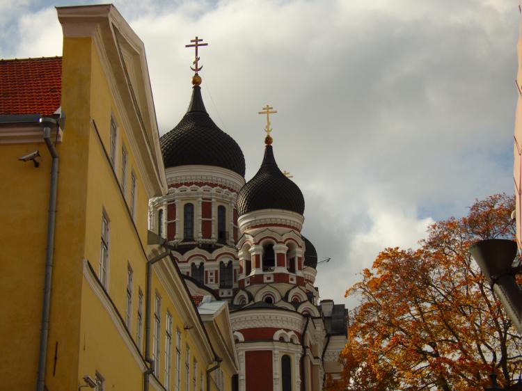 A red, Russian-style church with domed roofs emerging from behind a pastel yellow house