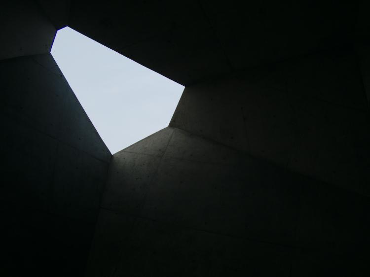 Interior of a large concrete sculpture with a polygon-shaped opening at the top letting light in from above