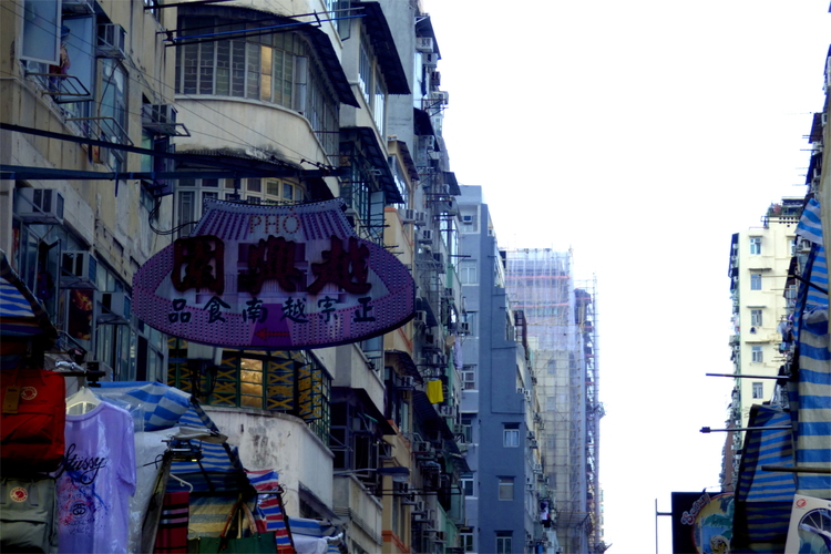 A sign in the shape of an UFO with some Chinese characters and the word 'Pho' hanging off the side of a building