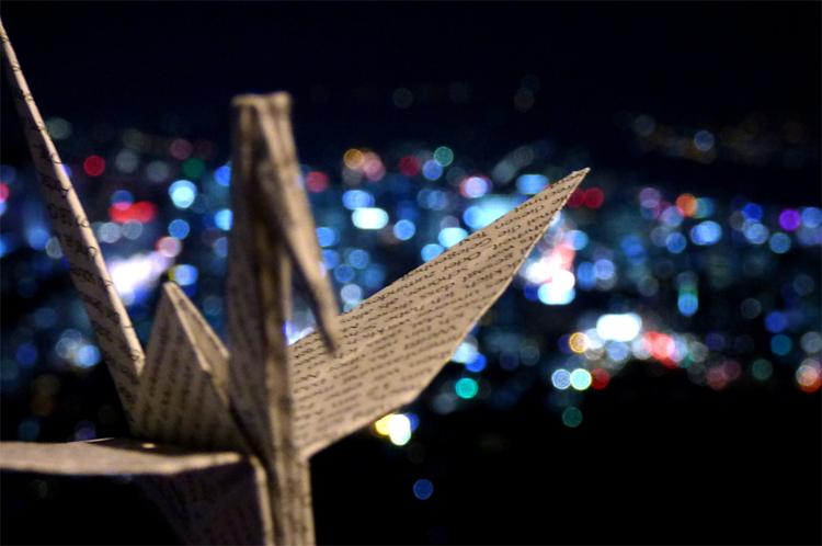 An origami crane in front of the blurred city lights of Seoul at night