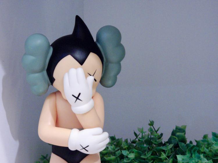 Close-up of a cartoon-style plastic figure with white gloves and black hair doing a face-palm pose