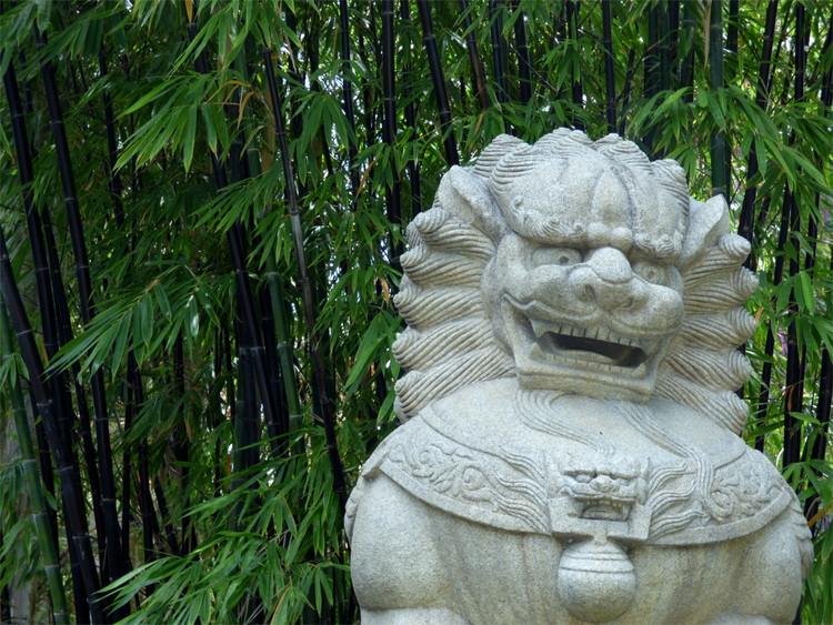 A white stone statue of a lion in front of bamboo plants