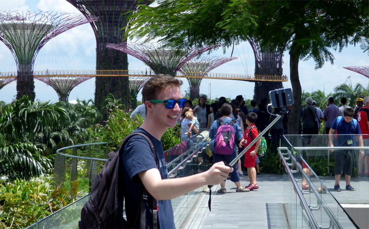 Jan, wearing sunglasses and a backpack, taking a selfie with a selfie stick in front of some 'Supertrees'
