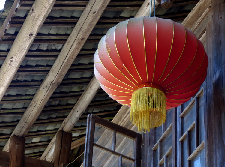 A large red-and-yellow Chinese lantern hanging from a simple wooden singled roof