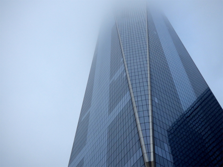 The blue glass facade of the One World Trade Center skyscraper vanishing into fog