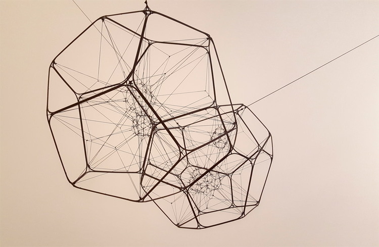 An abstract, geometric wireframe sculpture suspended from the ceiling