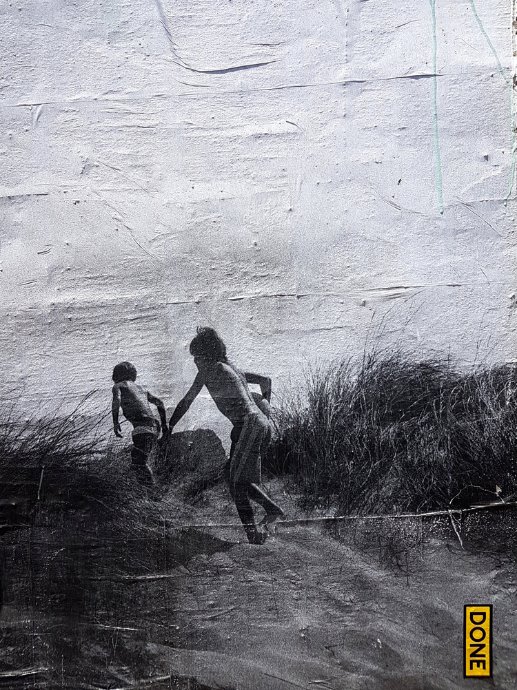 A black-and-white mural of two children running off on a beach dune with the word 'done' in a yellow box in the corner